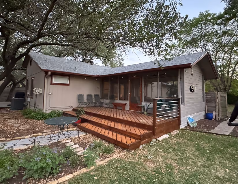 Backyard deck with wooden stairs, metal table, chairs, and screened porch attached to a house.