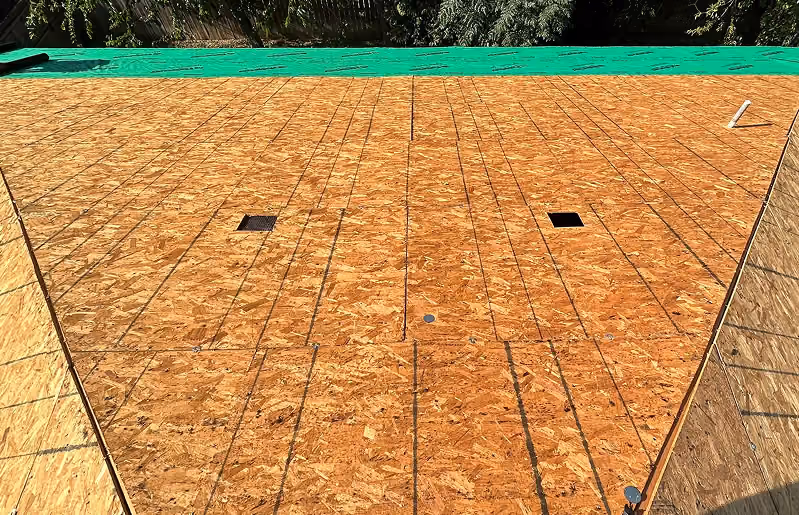 Plywood roof decking installed with two black vents and green tarpaulin at top edge.