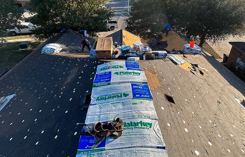 Workers installing new roofing materials on a large house roof under bright daylight.