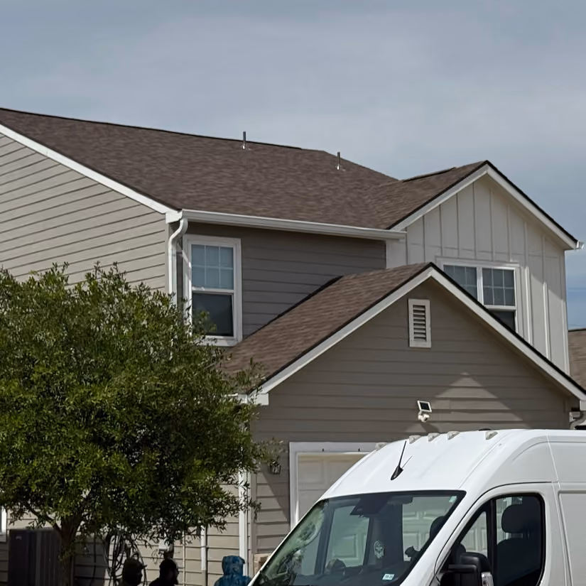 Suburban house with gray siding and a white van parked in front near a leafy green tree.