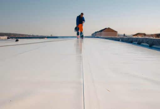 Worker smoothing seams on a new white commercial roofing membrane outdoors.