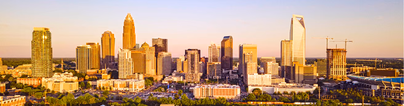 Sunlit aerial view of a city skyline with tall buildings and greenery at sunset.