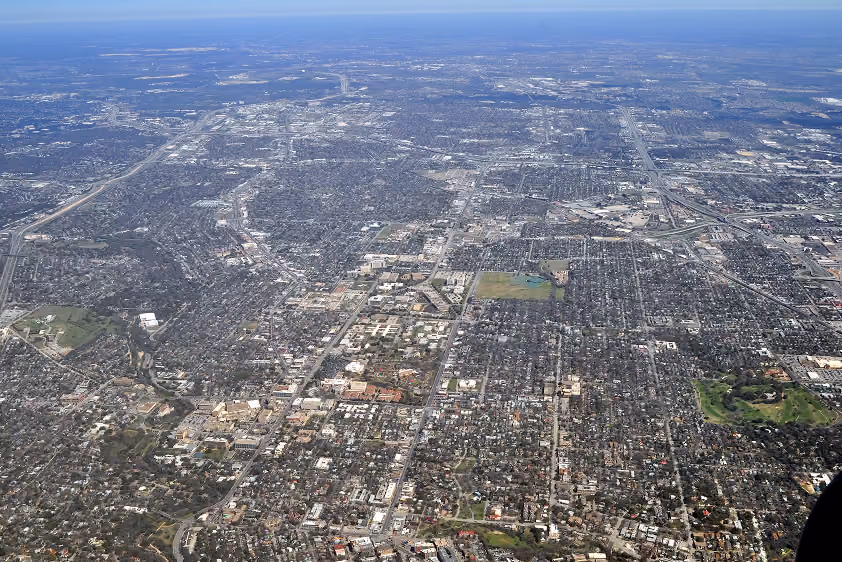Aerial view of a sprawling urban area with roads, buildings, and patches of greenery under clear skies.