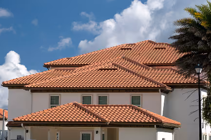 White house with terracotta clay tile roof under a partly cloudy blue sky.