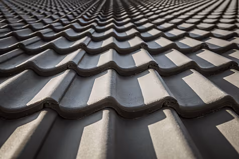 Close-up of dark gray synthetic roofing tiles arranged in rows with light and shadows.