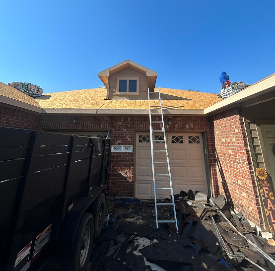 House roof under repair with ladder leaning on garage and worker stacking shingles on roof.