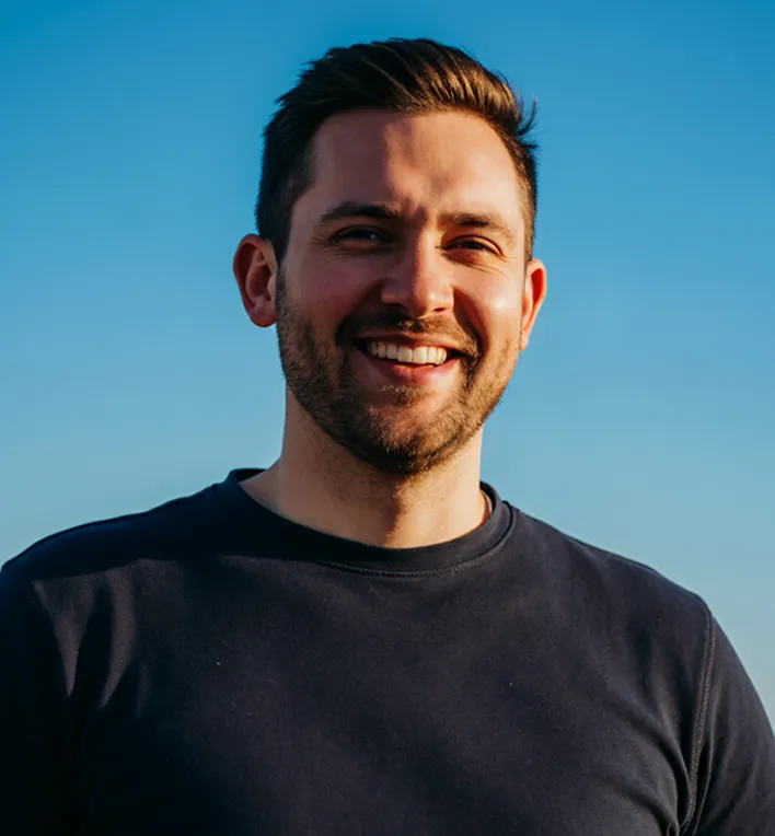 Portrait of a smiling bearded man in a dark shirt against a blue sky