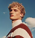 Portrait of a blonde man wearing a red and white sweater against a cloudy sky