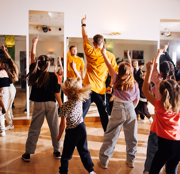 Ein Tanzlehrer zeigt einer Gruppe Kinder Tanzschritte vor einem Spiegel.