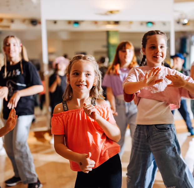 Eine Gruppe Kinder üben gemeinsam Tanzschritte vor einem Spiegel.
