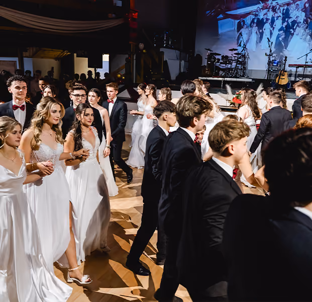 Jugendliche Tanzpaare in einem festlichen Ballsaal.