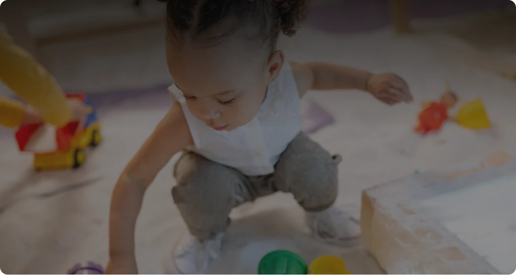 Young child squatting and playing with colorful toys on the floor.