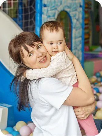 Woman holding a toddler beside an indoor ball pit