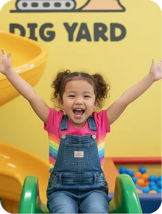 Smiling girl raising her arms on a play structure at Dig Yard