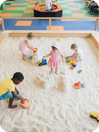 Children digging and playing with buckets in a large indoor sandbox
