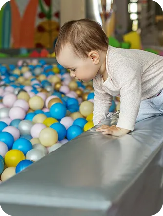 Toddler leaning over the padded edge of a colorful ball pit