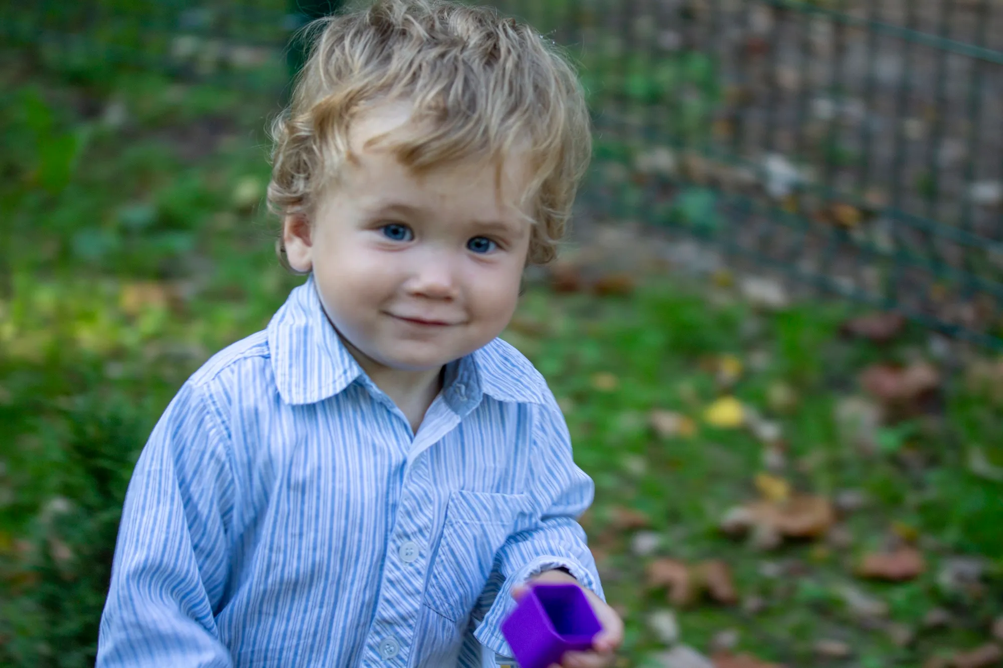 Young boy in a striped shirt holding a purple toy outdoors