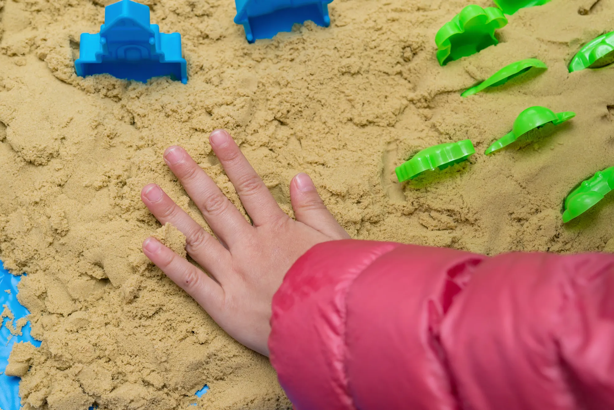Child pressing a hand into sand beside colorful sand molds