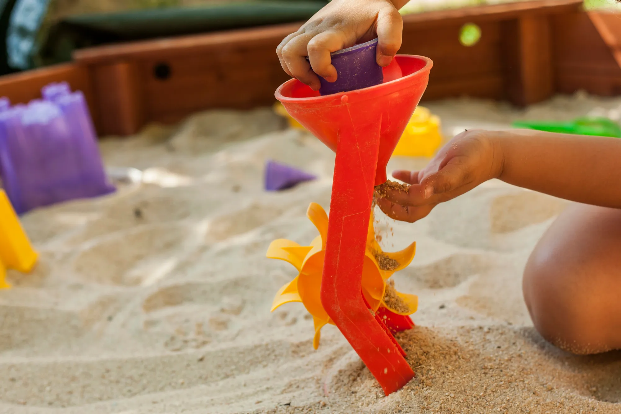 Child pouring sand through a red sand wheel