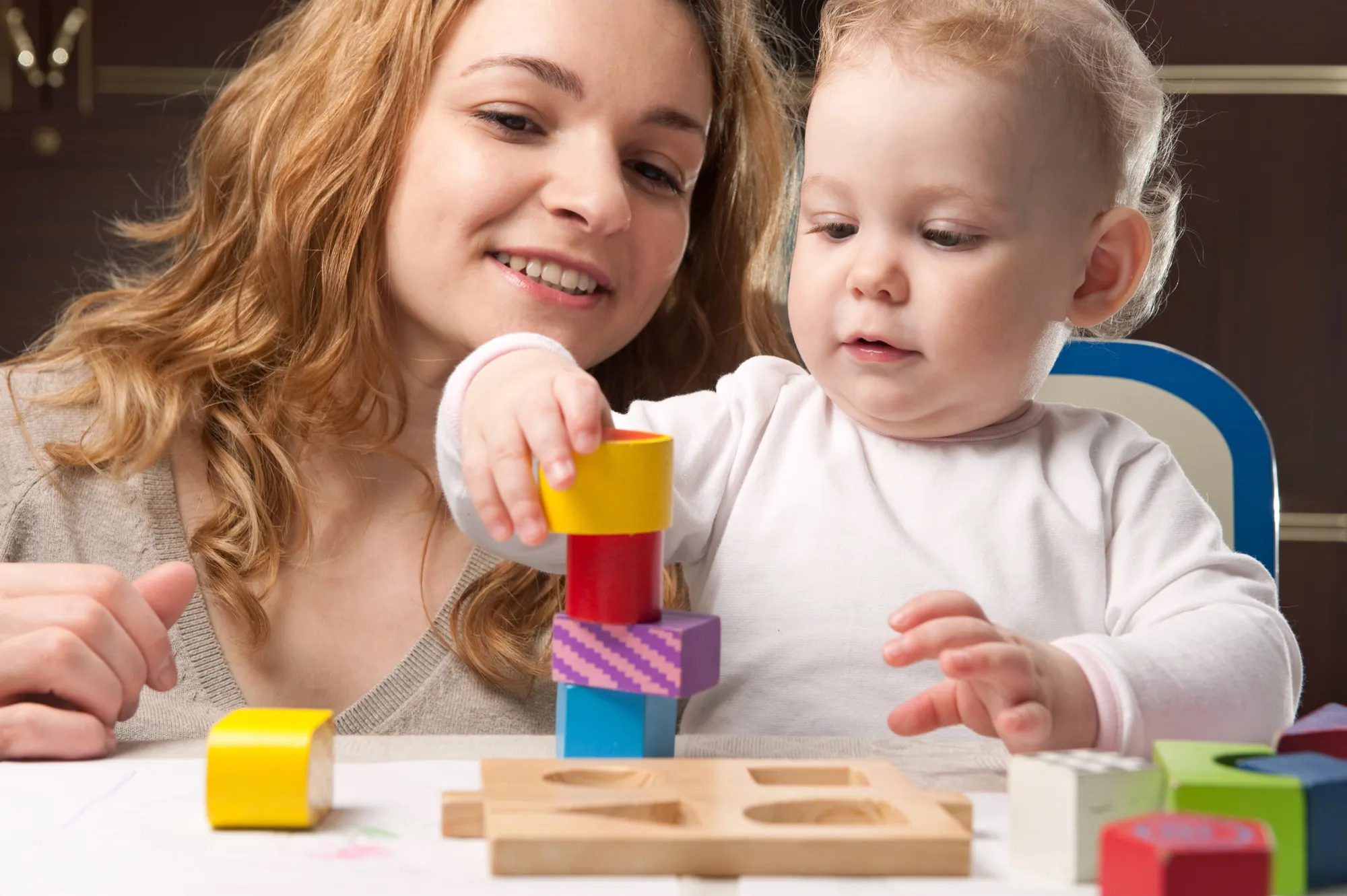 Woman watching a toddler stack colorful wooden blocks
