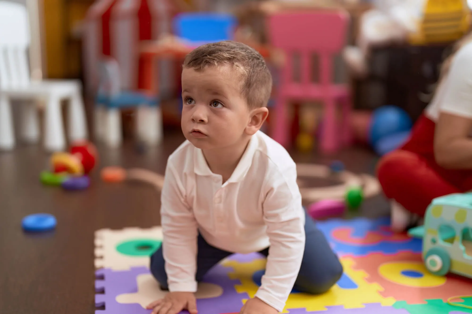 Young boy kneeling on a colorful alphabet play mat among toys