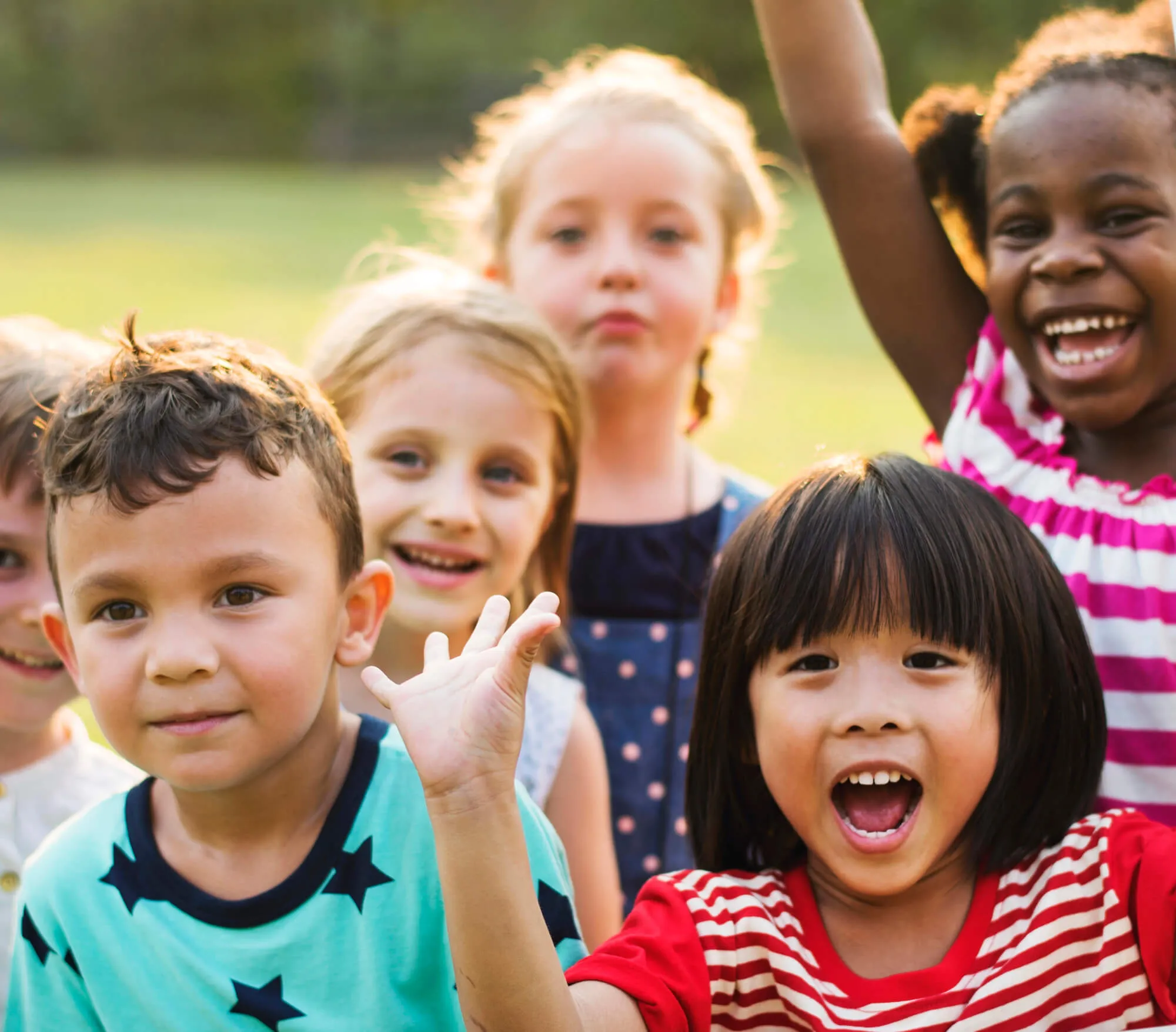 Group of children smiling and waving outdoors