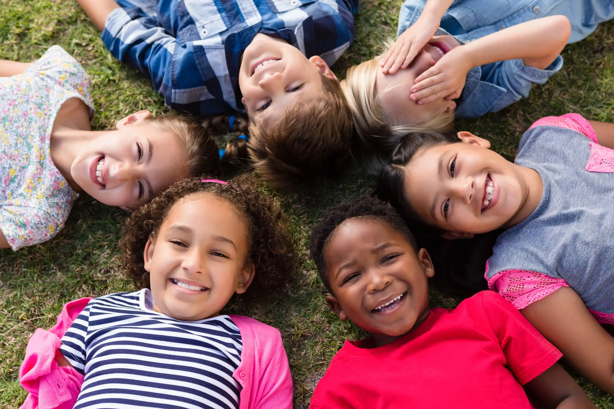 Six smiling children lying in a circle on the grass