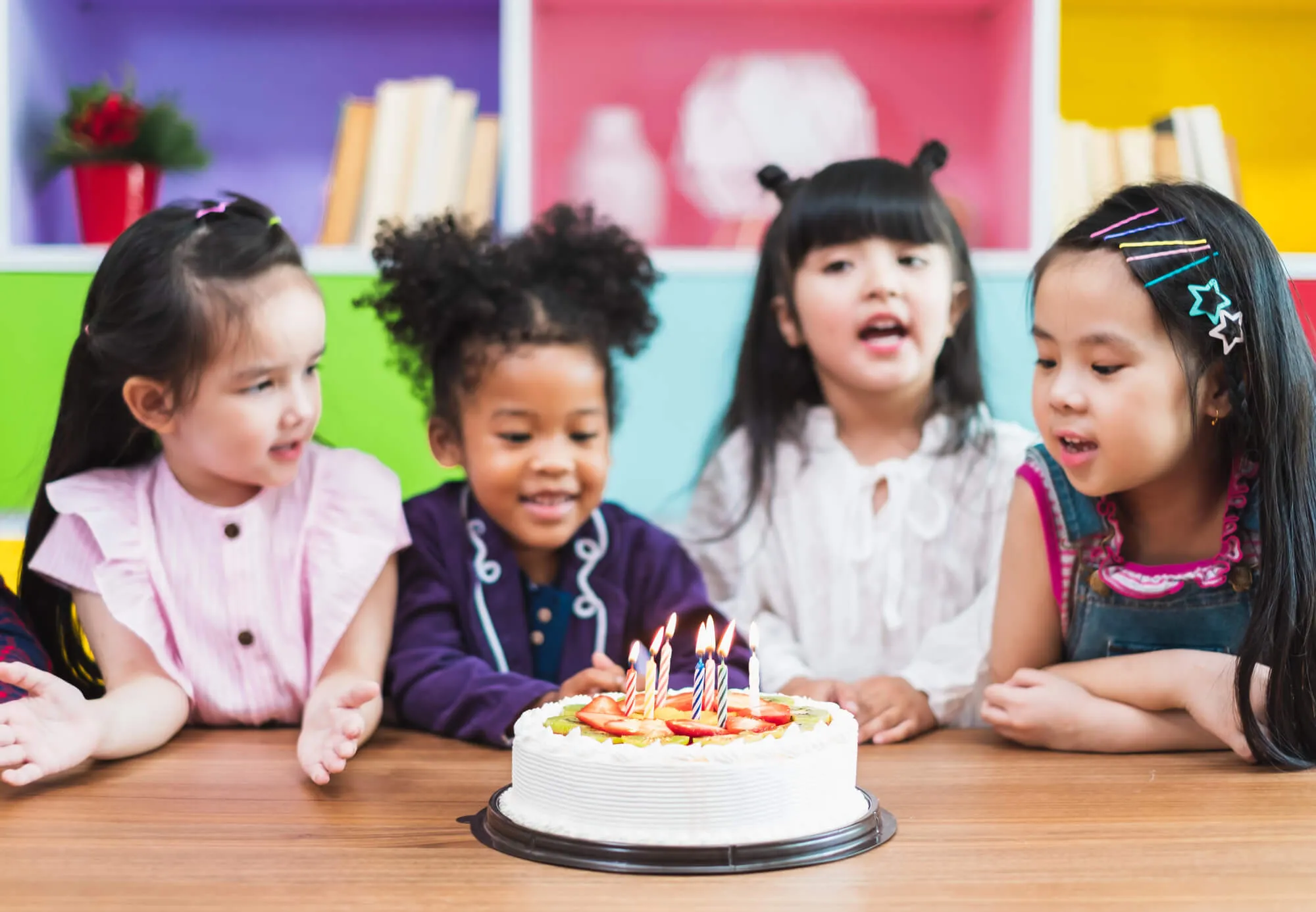 Four girls gathered around a birthday cake with lit candles