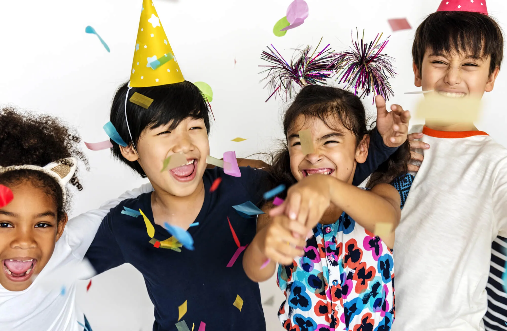 Excited children in party hats celebrating as confetti falls around them