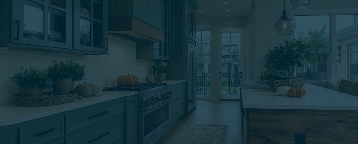 Modern kitchen with white countertops, wood cabinets, stove, plants, and pumpkins on counters.