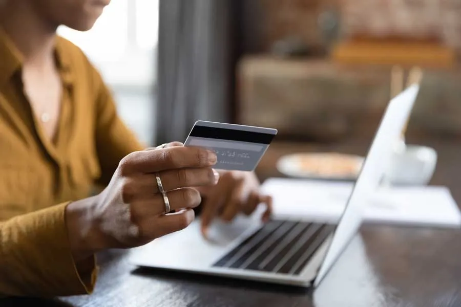 Person holding a credit card and typing on a laptop keyboard at a table.
