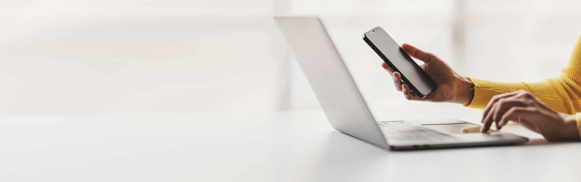 Person using a smartphone in one hand and typing on a laptop keyboard with the other hand.