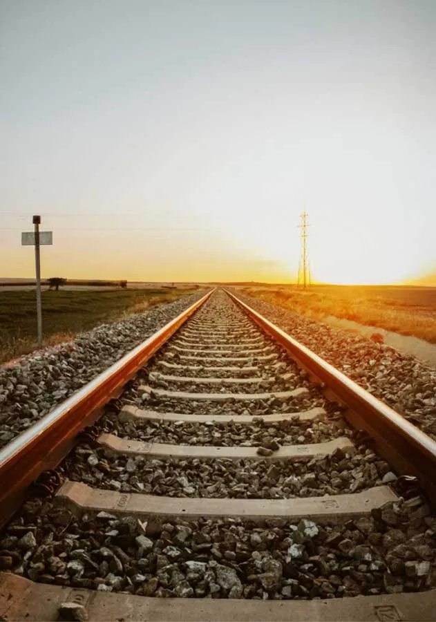 Railroad tracks stretching into the horizon at sunset with grassy fields on either side.