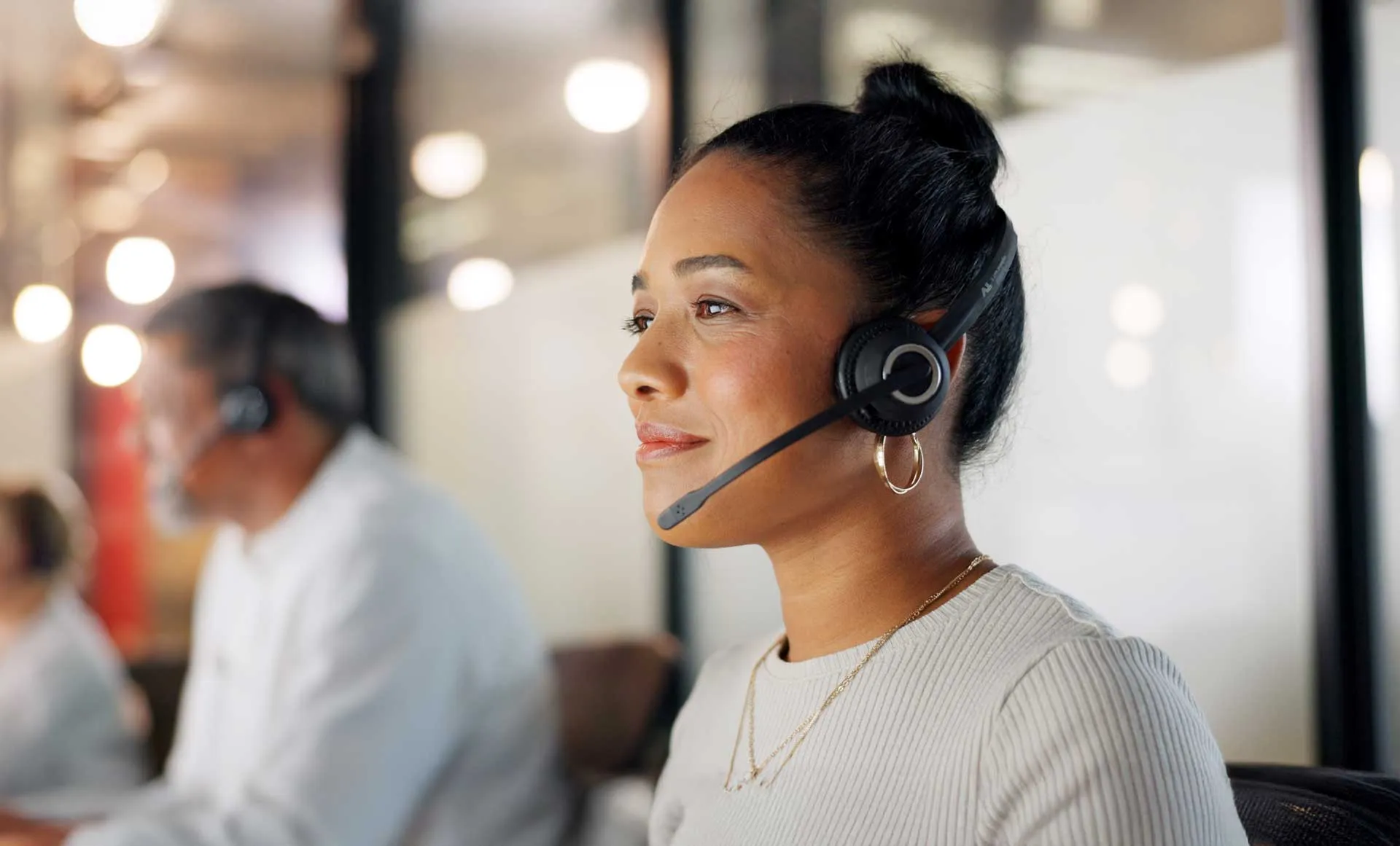 Woman with headset working at a call center with colleagues in background.