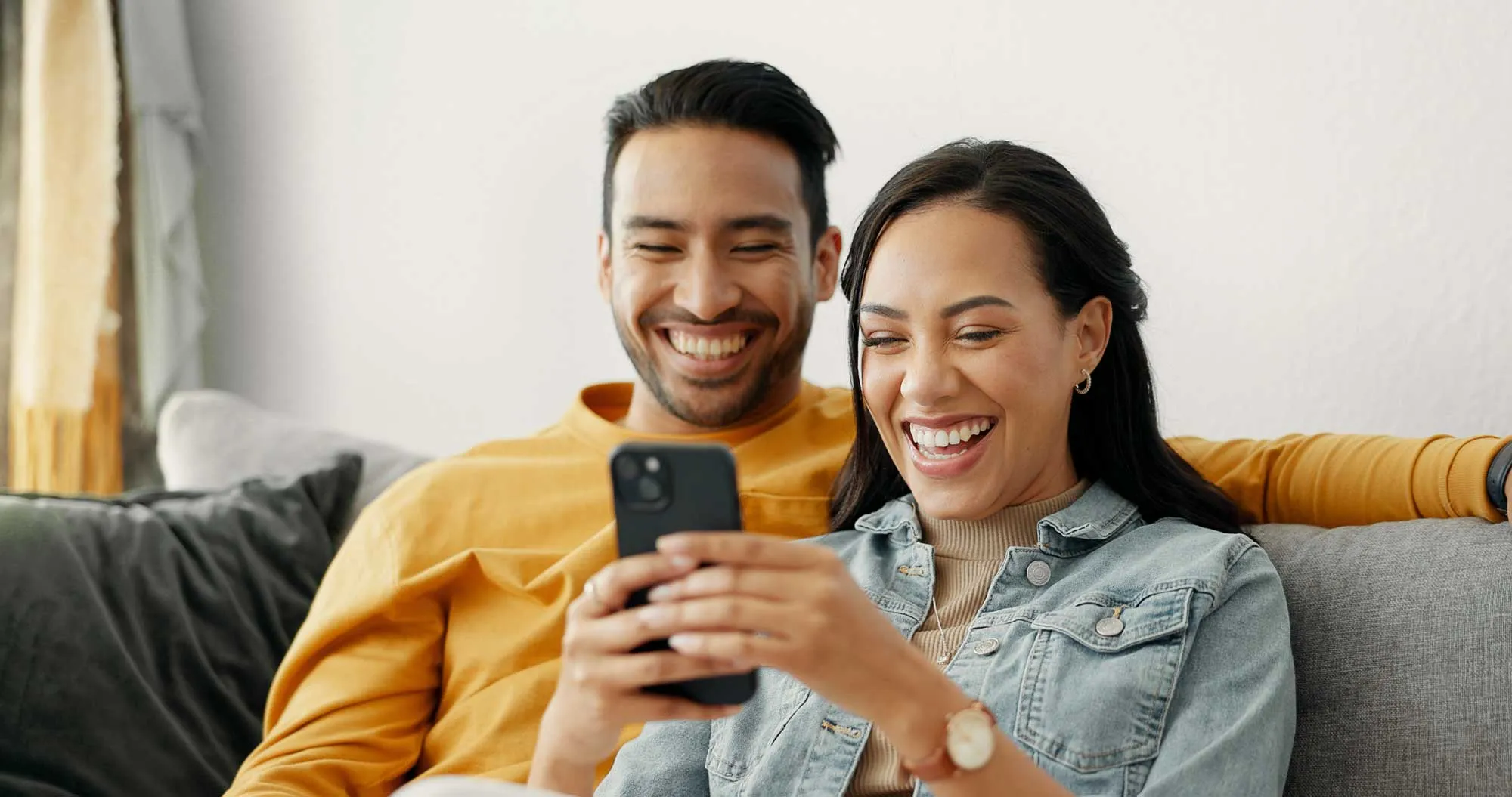 Smiling couple sitting on couch looking at a smartphone together.