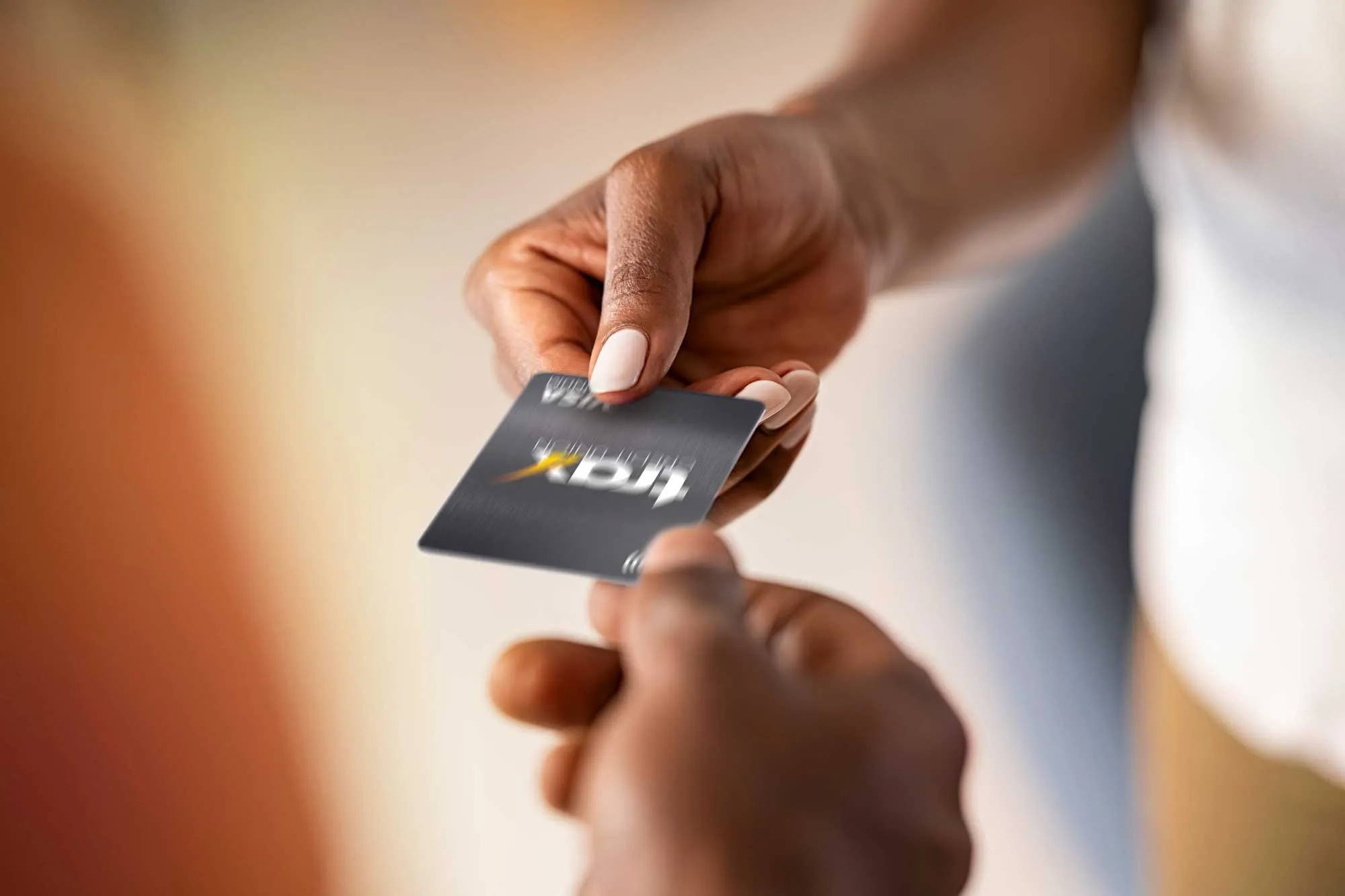 Person handing a black credit card to another person indoors with blurred background.