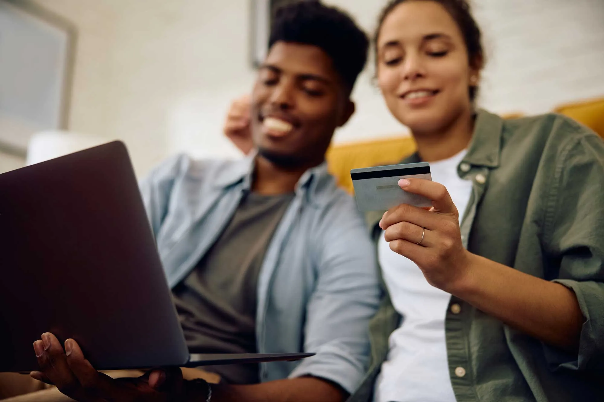 Smiling couple using a laptop and credit card for online shopping at home.