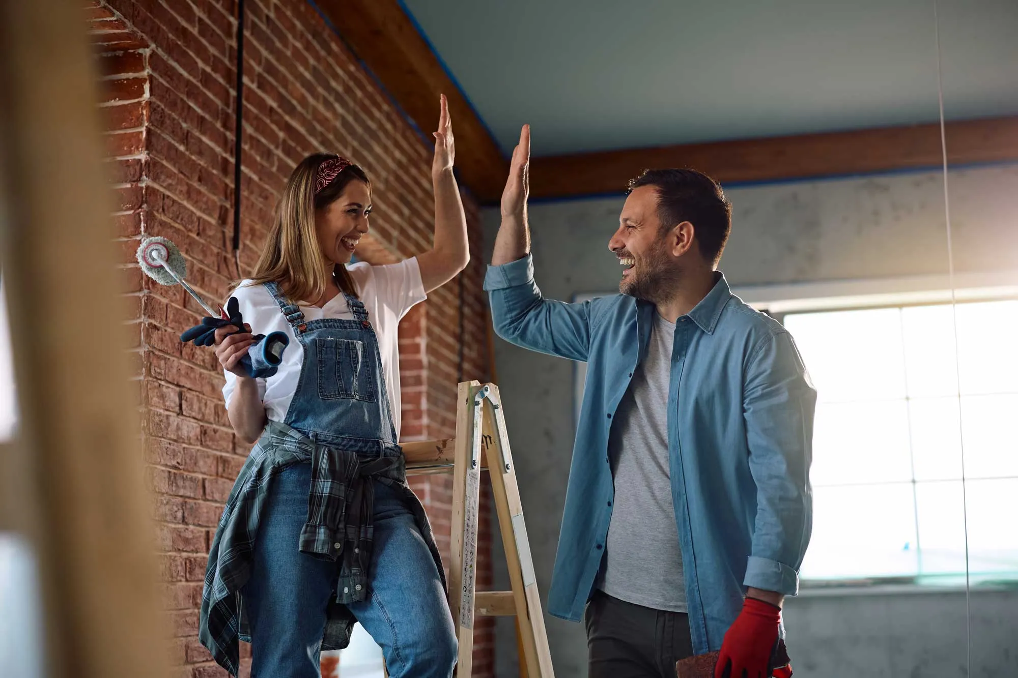 Man and woman with painting tools smiling and giving a high-five during home renovation.