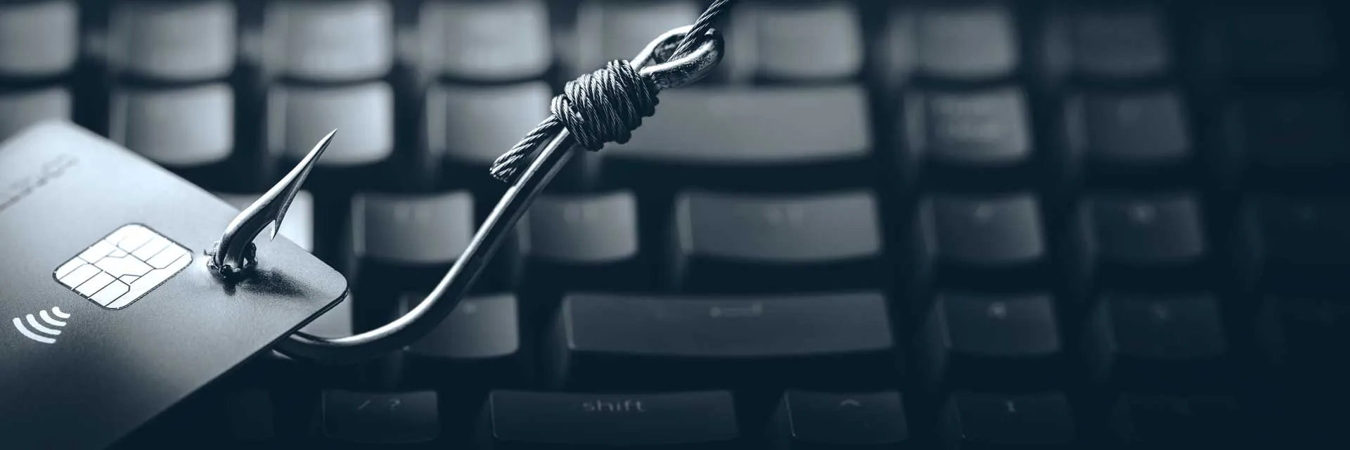 Credit card pierced by a fishing hook over a keyboard symbolizing online fraud or phishing attack.
