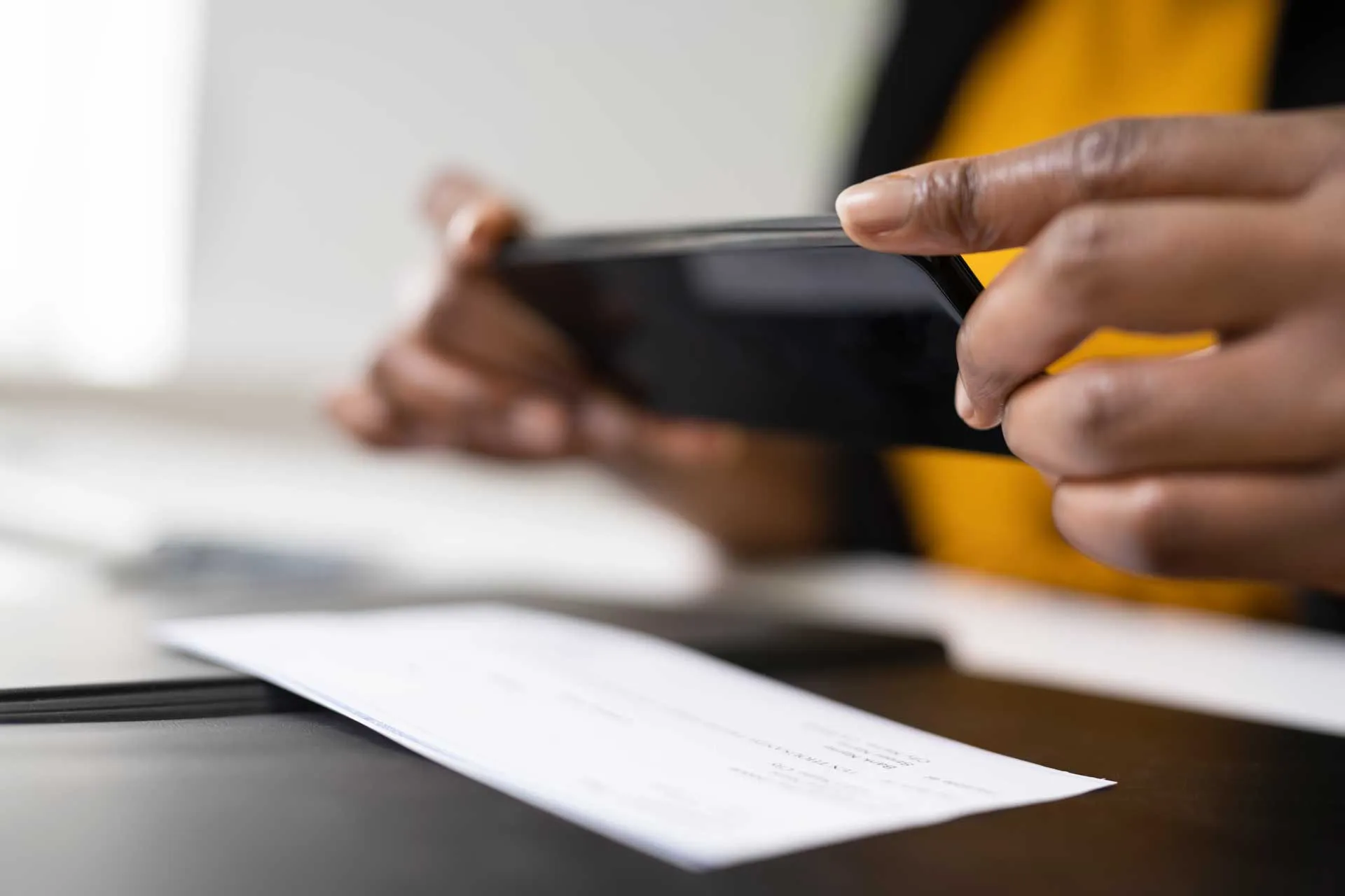 Person using a smartphone to scan a document on a table for remote deposit.