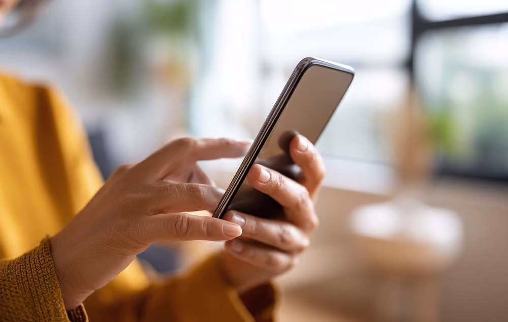 Hands holding a smart phone in a brightly lit room.