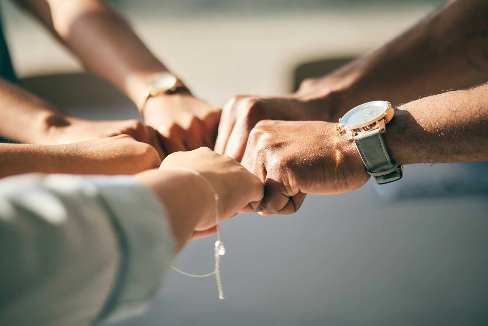 Five diverse hands joined in a circle performing fist bump teamwork gesture.
