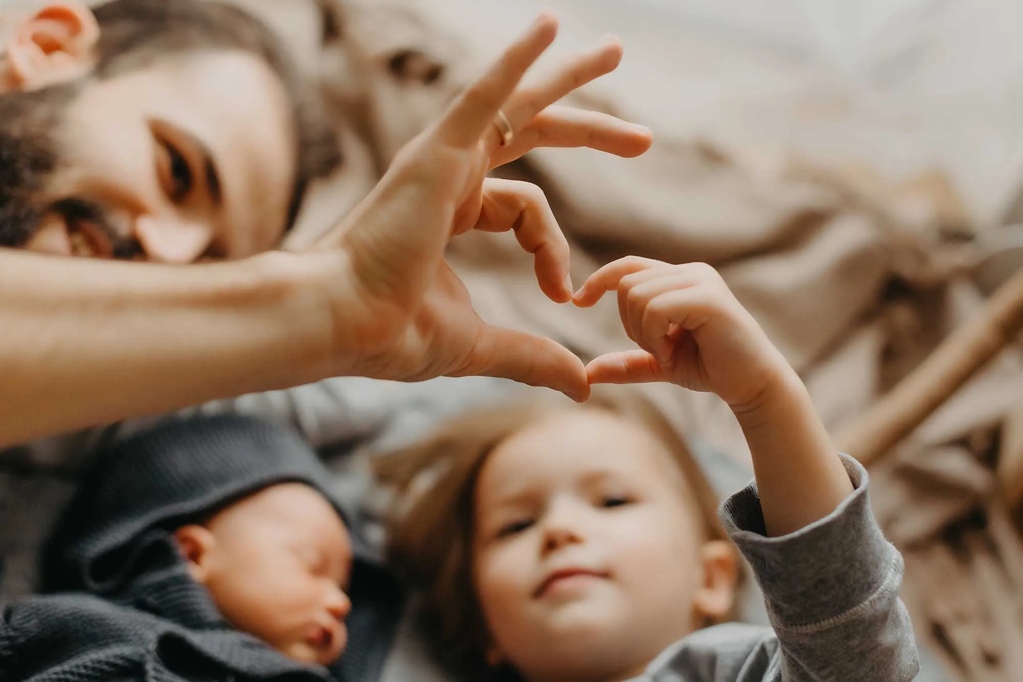 Man and child lying down forming a heart shape with their hands near a sleeping baby.