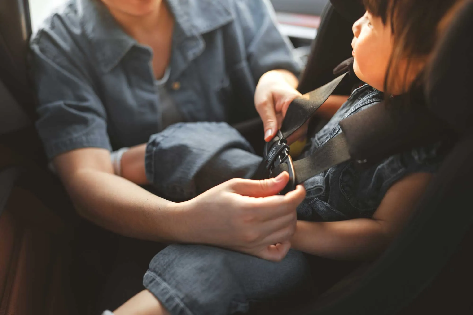 Adult fastening a seatbelt for a young child sitting in a car seat.