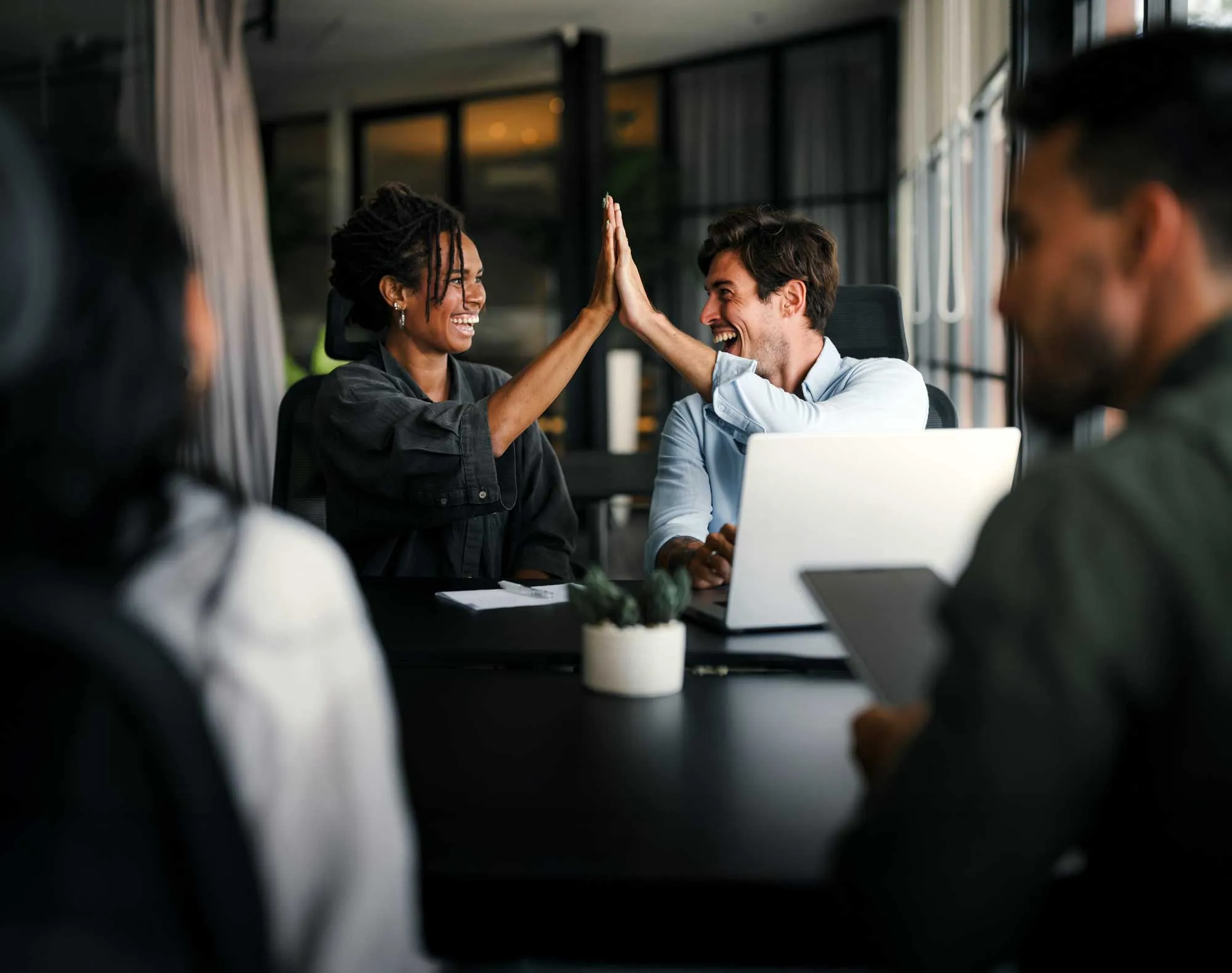 Two colleagues smiling and giving a high five during a meeting in a modern office.