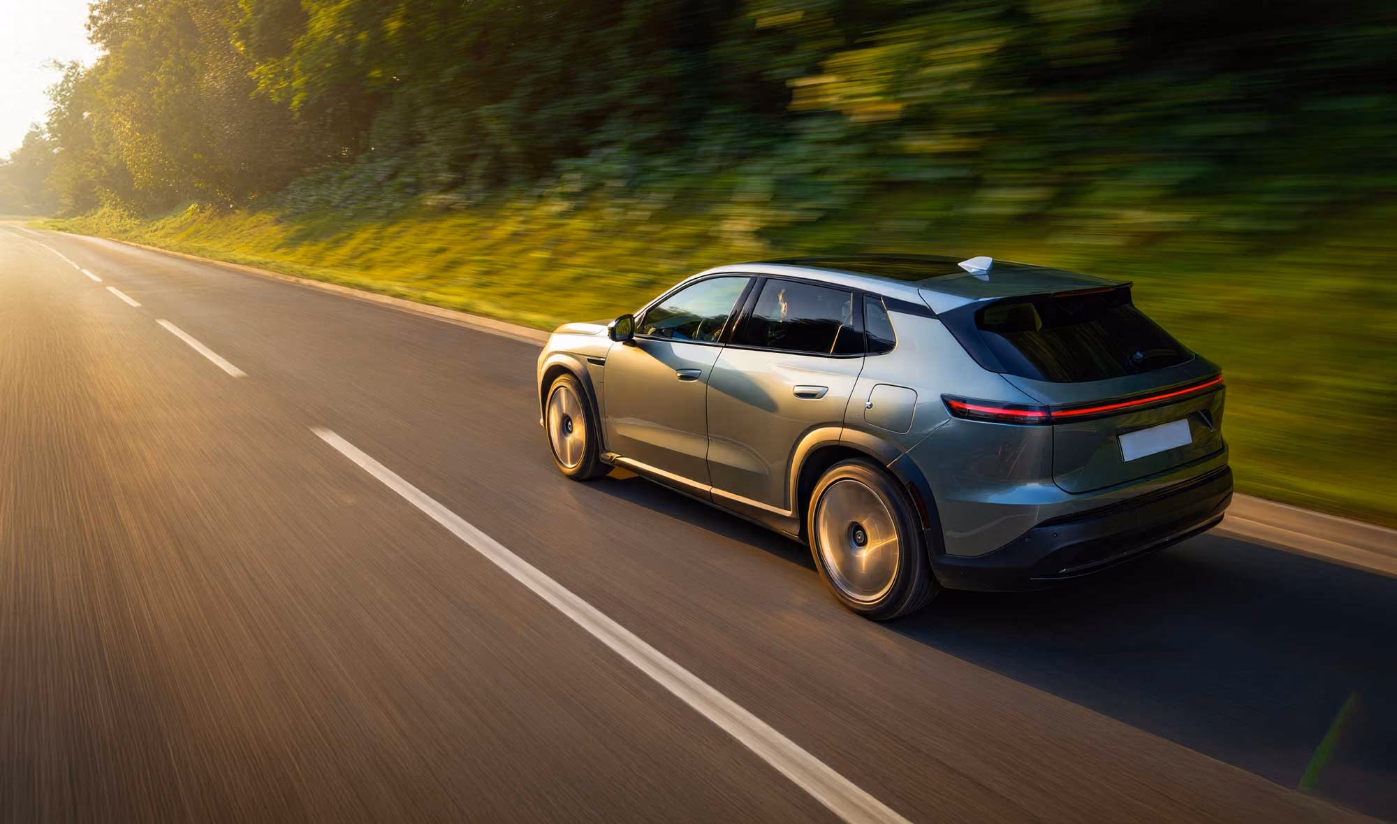 Silver SUV driving on a sunlit road with trees and greenery on the roadside.