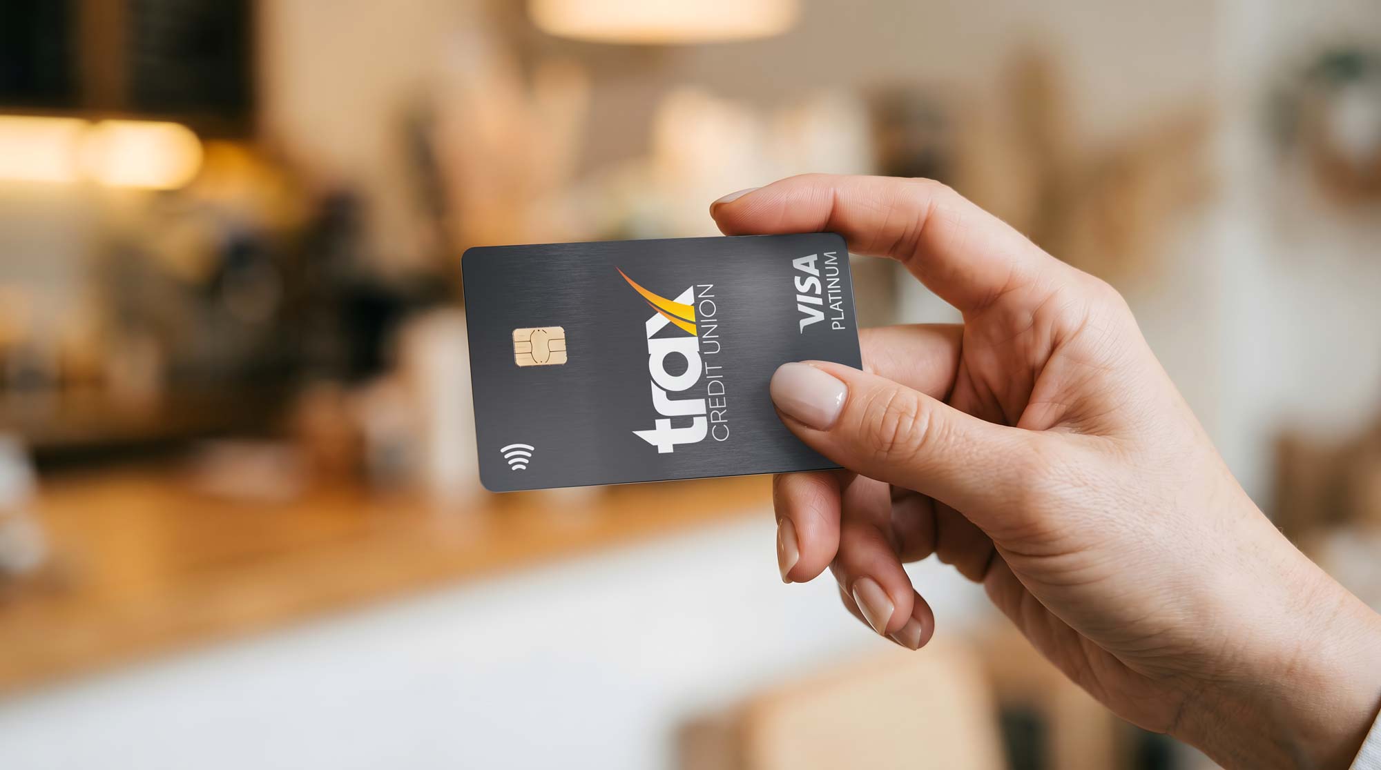 Hand holding a black Travel Credit Union Visa Platinum credit card with contactless payment symbol, chip, and logo visible.