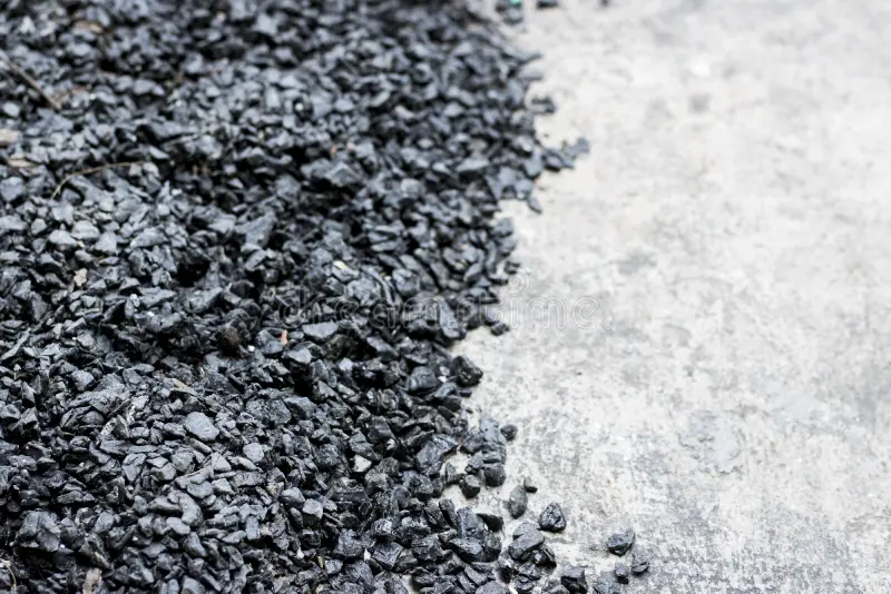Close-up of black crushed stones or gravel on the left side next to a gray concrete surface.