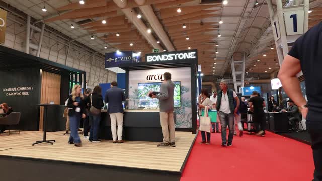 People visiting an indoor trade show booth with Bondstone and Revito signs and a red carpet aisle.