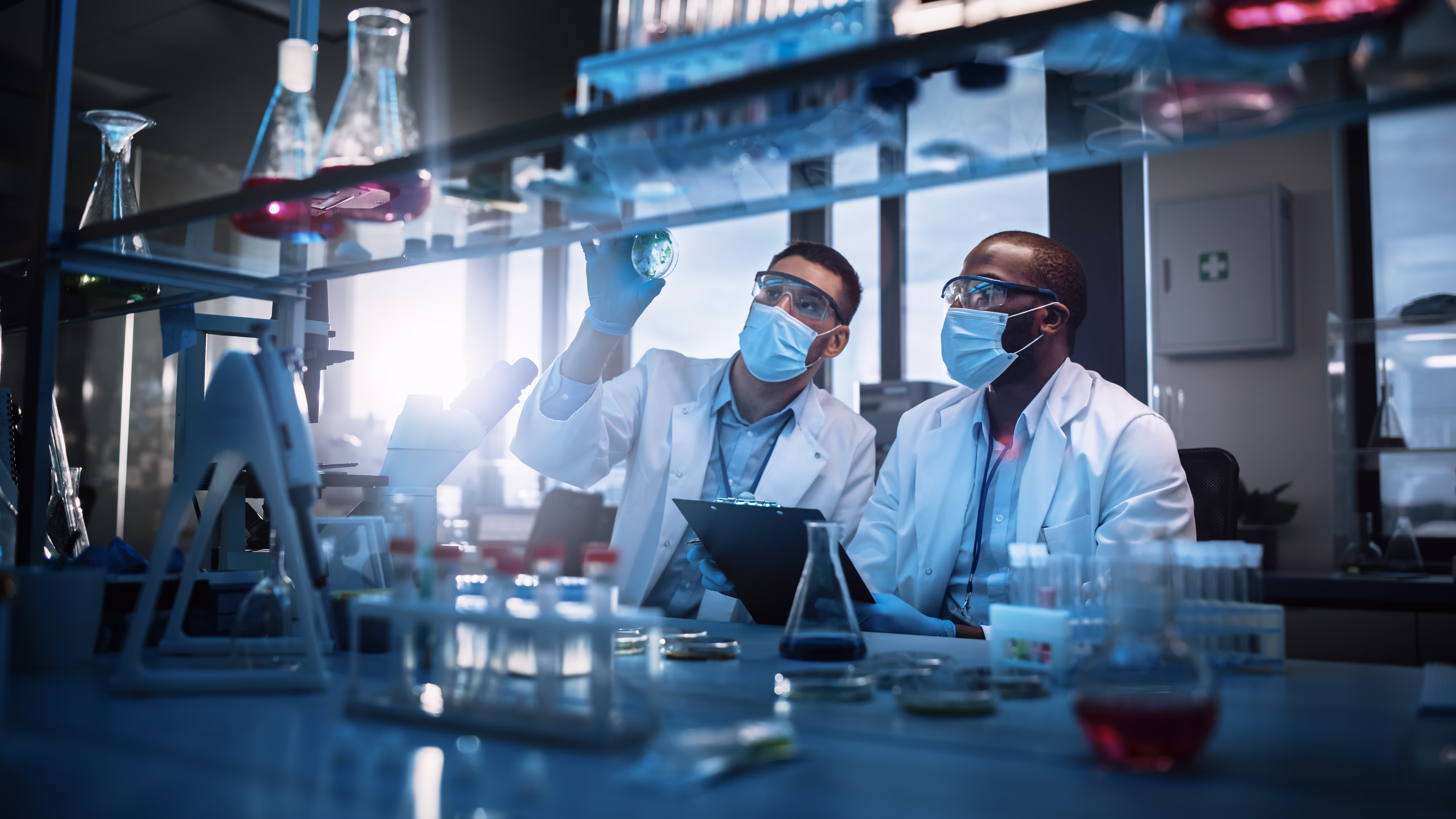 Two scientists in lab coats and masks reviewing results on a tablet in a laboratory